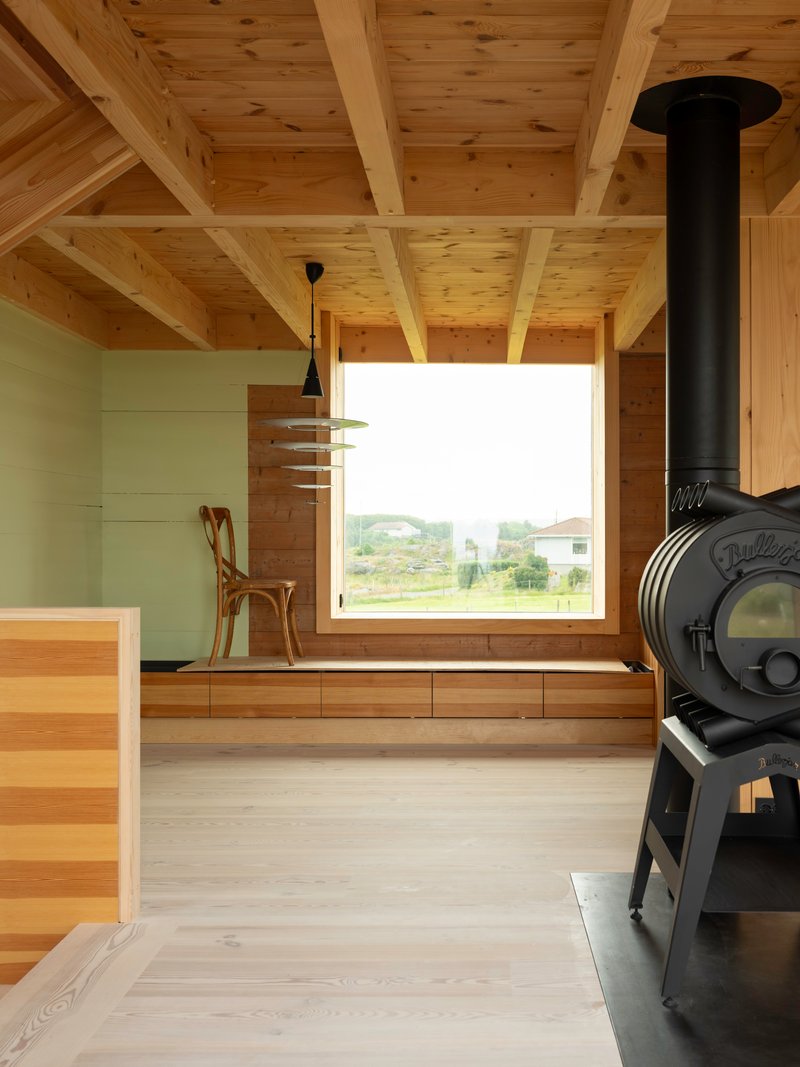 Interior with exposed timber ceiling beams and a black wood stove beside a window seat overlooking green fields