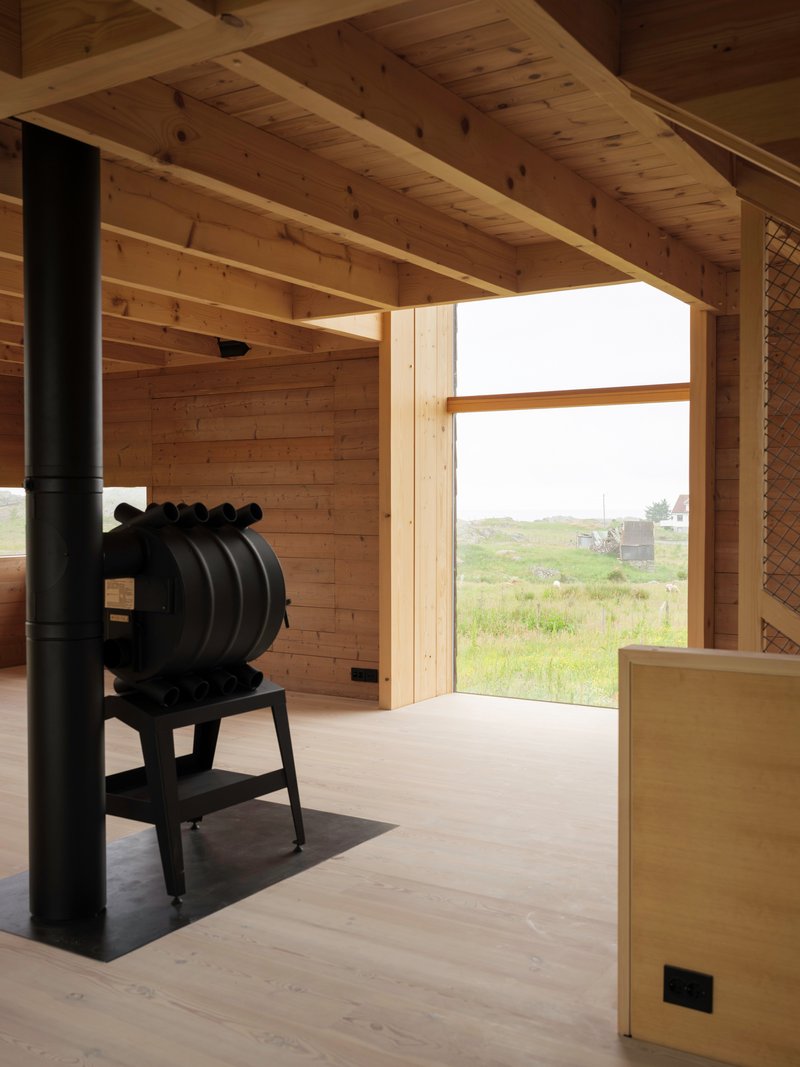 Black cast iron stove on a metal hearth beneath a timber beam ceiling with landscape view beyond
