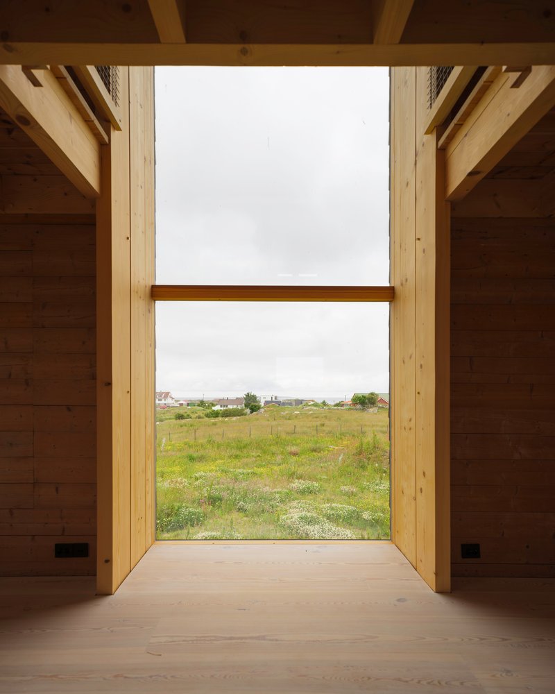 Floor-to-ceiling window framing view of green field with scattered houses under overcast sky