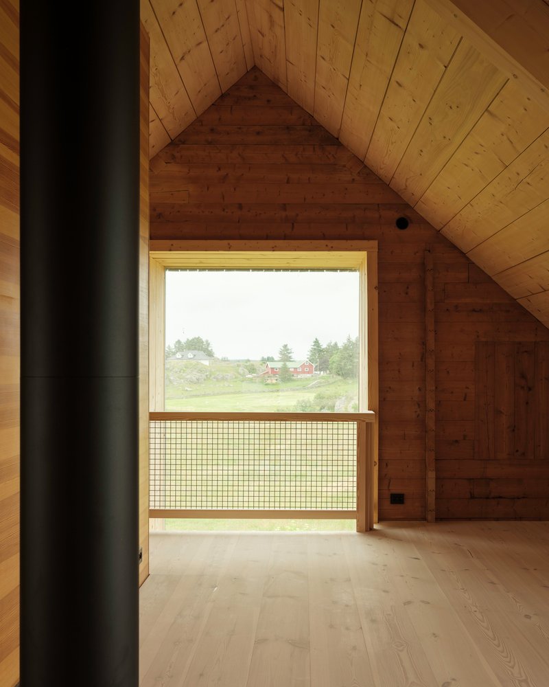 Upper floor timber room with gabled ceiling and mesh safety railing at window overlooking fields
