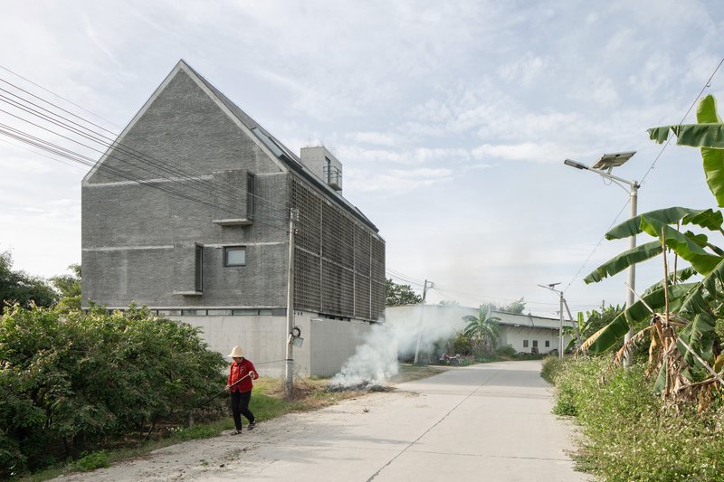 Street view of the house-shaped concrete volume with perforated brick screen and a person walking past