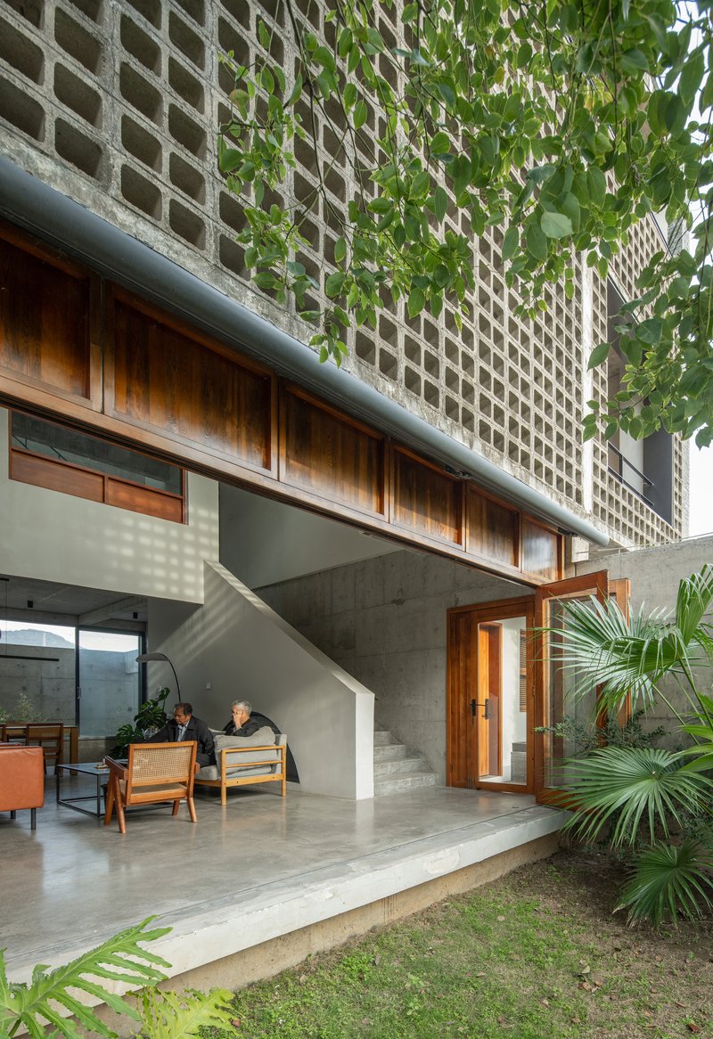 Covered terrace with concrete overhang, timber joinery, and perforated brick wall framing a planted courtyard