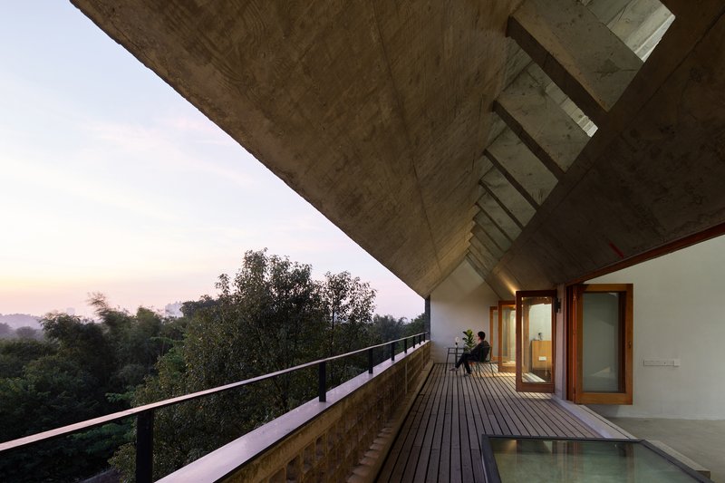 Covered timber deck with concrete overhang and steel railing overlooking forested landscape at dusk