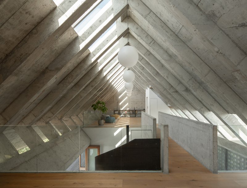 Vaulted concrete ceiling with rhythmic beams and skylights above a lofted timber floor with suspended globe pendants