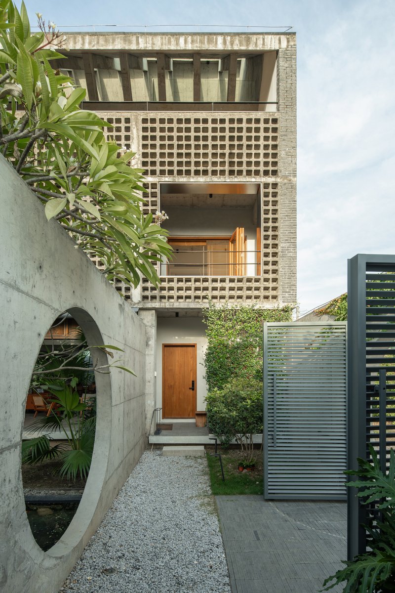 Entry courtyard with perforated brick facade and timber door framed by concrete walls and plantings