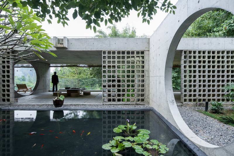 Koi pond with lotus plants beneath concrete arches and breeze block walls with a figure standing beyond