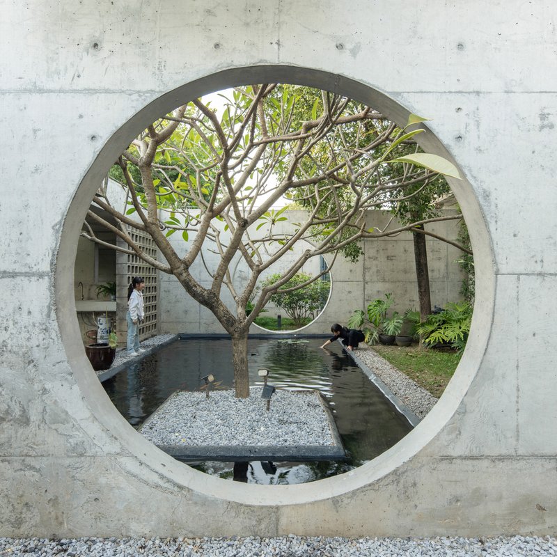 Circular concrete opening framing a tree and reflecting pool with figures tending the water
