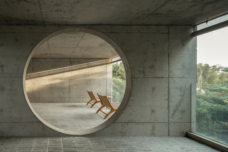 Circular concrete portal framing two wooden chairs on a terrace overlooking dense foliage