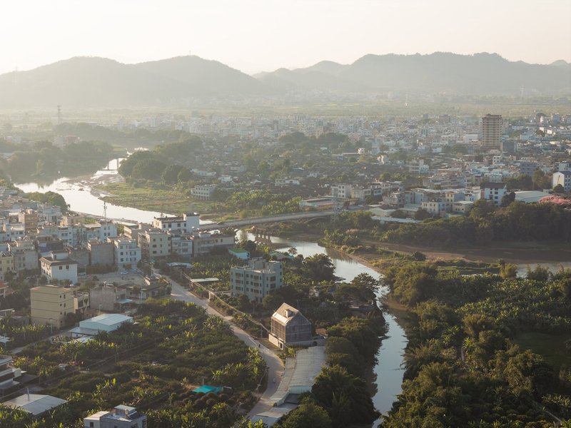 Aerial view of a gable-roofed structure nestled along a winding river with mountains in the distance at dusk