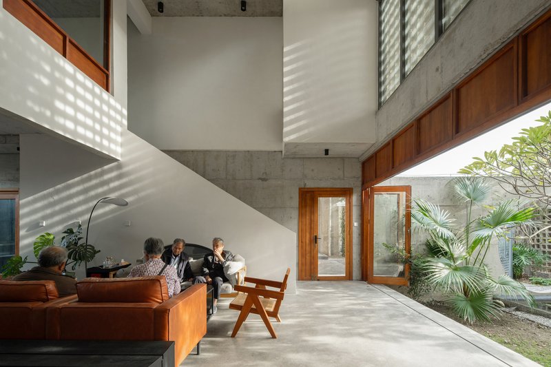 Double-height living room with concrete ceiling, timber doors and patterned light from perforated screens falling across white walls
