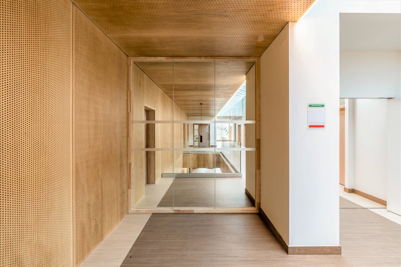 Perforated timber wall and ceiling lining a corridor with view through glass to interior spaces