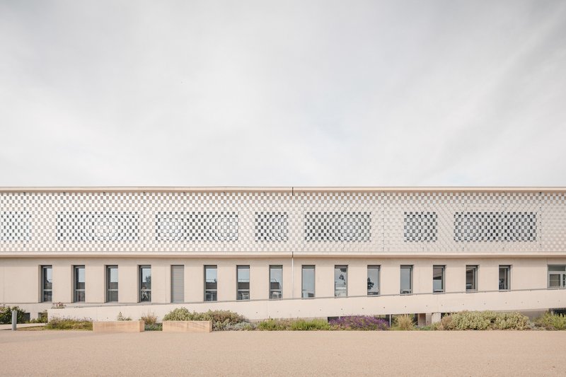 Facade with perforated upper screen and rhythmic window openings along the ground floor