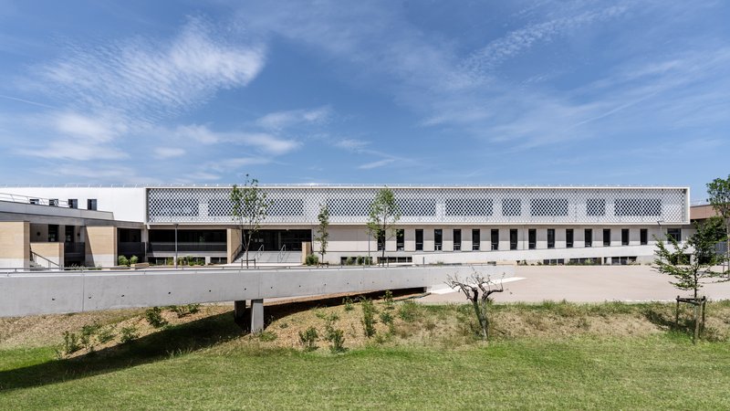 Long elevation with perforated metal screen above punched windows and concrete retaining wall below