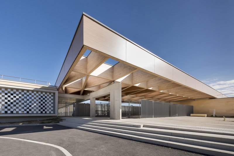 Covered entrance with exposed timber structure and concrete columns under a clear blue sky