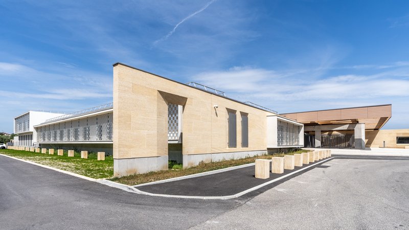 Corner view of the beige masonry facade with patterned screen panels and planted gravel beds