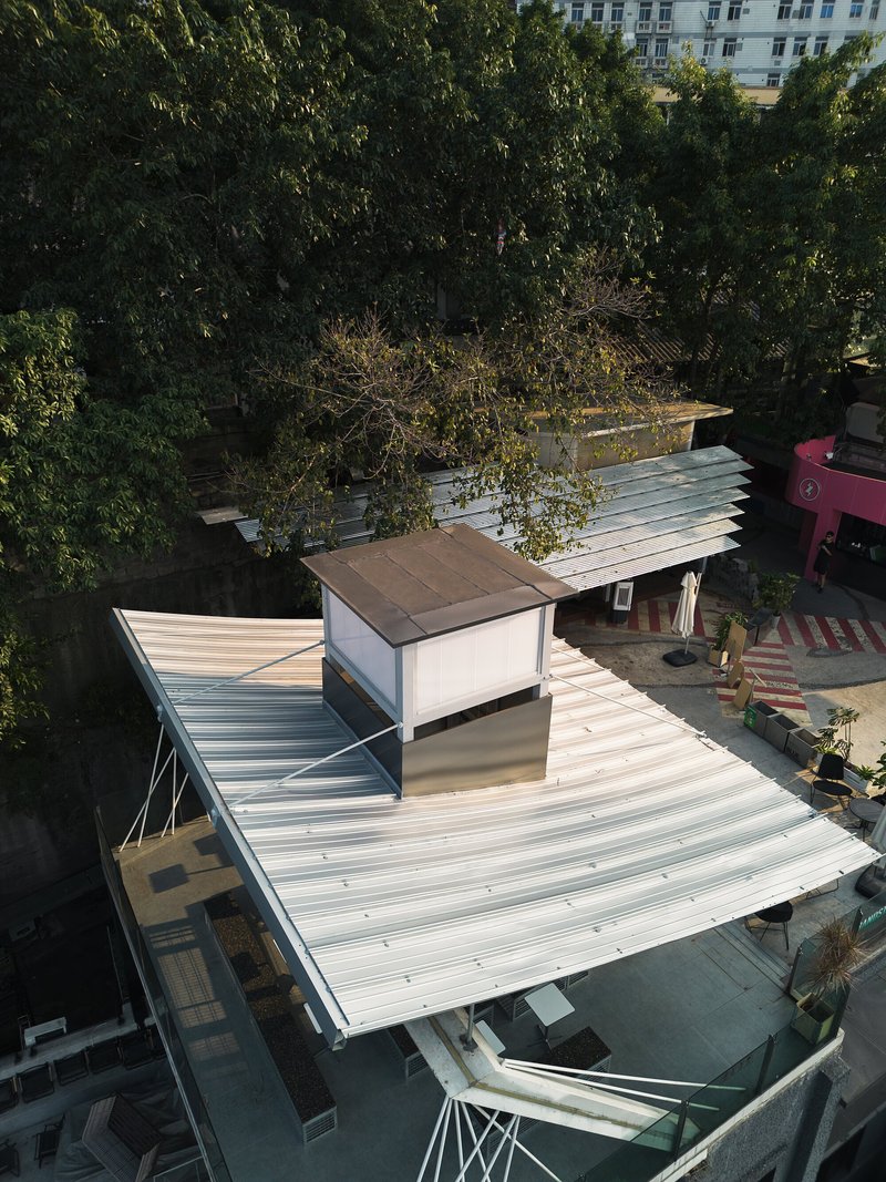 Overhead view of ribbed metal roof planes wrapping around a central skylit volume in morning light