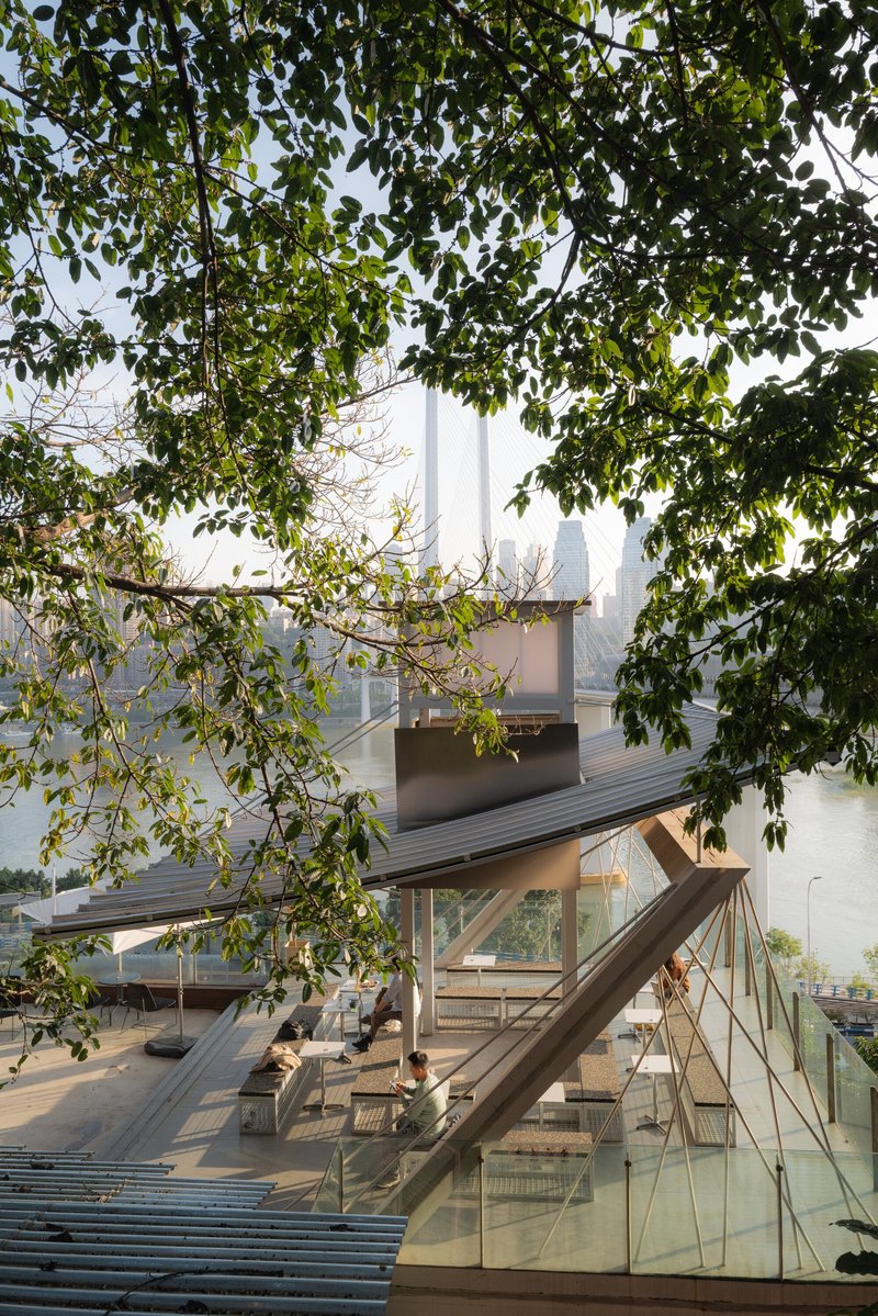 View through tree branches of an open timber pavilion with glass balustrade in morning haze