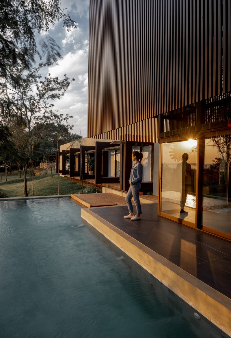 Two figures on the poolside deck at dusk beneath the vertical louvered facade and cloudy sky