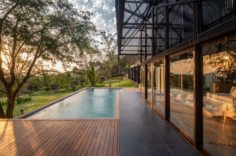 Timber deck terrace with lap pool alongside floor-to-ceiling glazing at golden hour