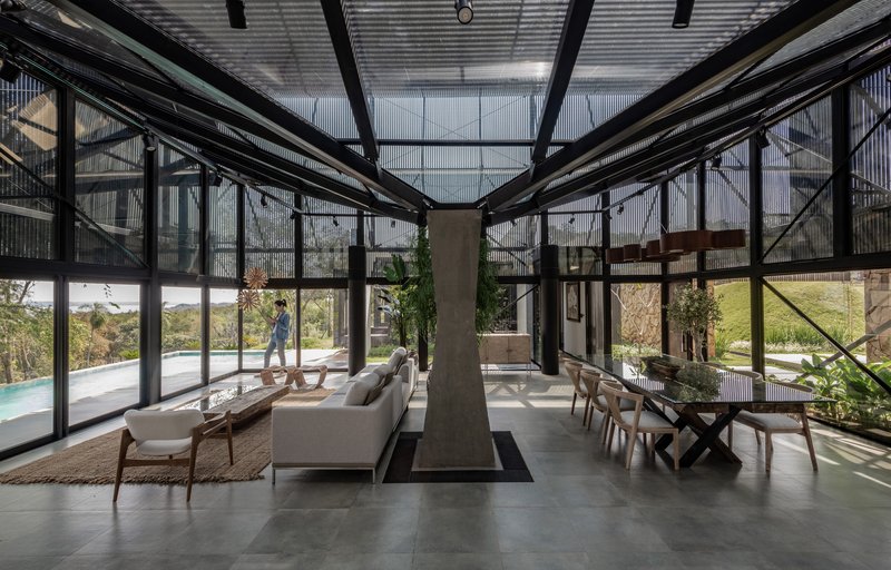 Glass-walled living area with exposed steel structure, central concrete fireplace and corrugated metal ceiling