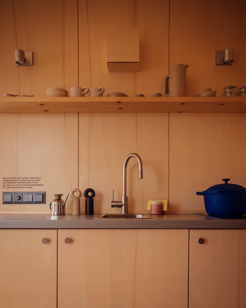 Kitchen counter with timber paneling, open shelf displaying ceramics, and gooseneck faucet at sink