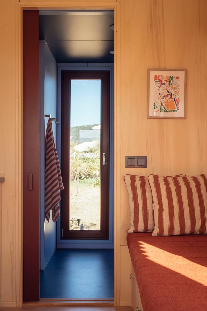View through plywood-lined doorway to a narrow bathroom with glazed door framing coastal landscape beyond