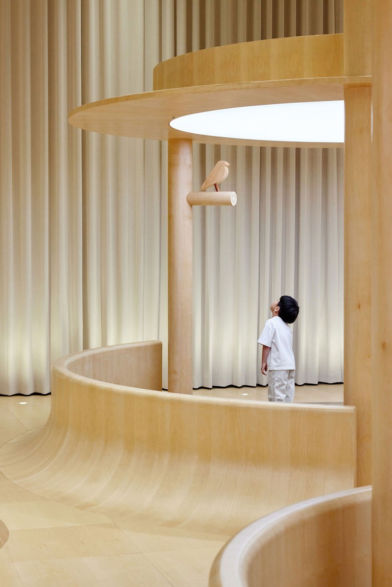 Multilevel plywood platforms with vertical curtain panels and a child standing beneath a perch