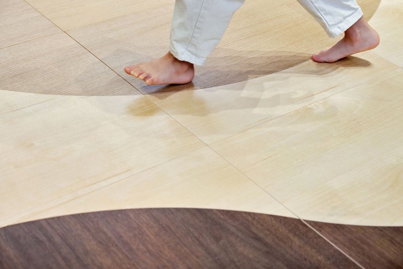 Close-up of bare feet crossing a curved floor joint between light and dark wood planks
