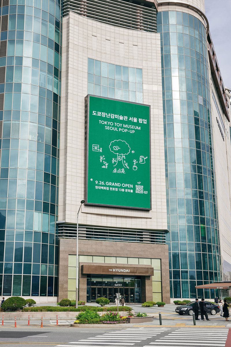 Curved glass and tile facade with large green signage banner above the ground-level entrance