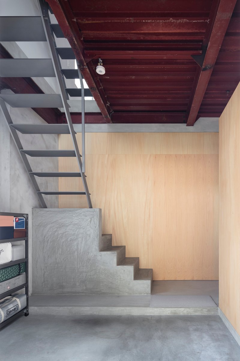 Concrete stair landing leading upward beneath dark timber ceiling and adjacent plywood wall