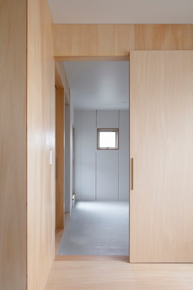 View through plywood-clad corridor toward a room with a centered square window
