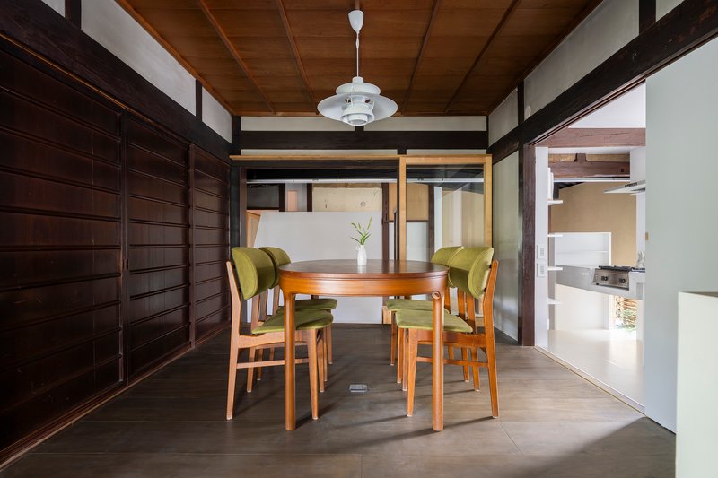 Dining area with timber table, green upholstered chairs and dark wood sliding wall panels under pendant light