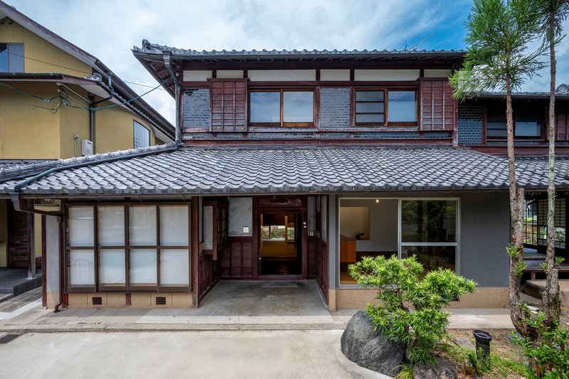 Street facade showing traditional tiled roof above timber framed windows and sliding screens with planted courtyard
