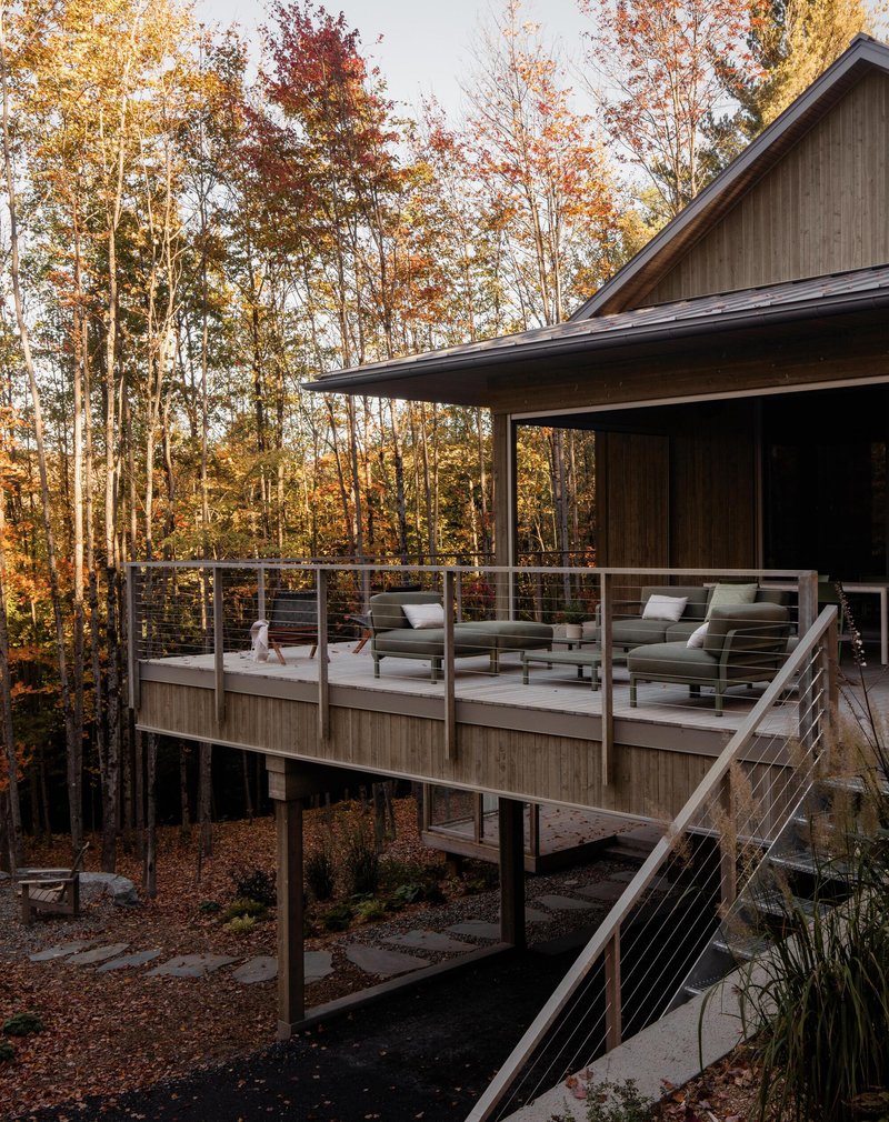 Elevated deck with cable railing and outdoor seating among autumn trees
