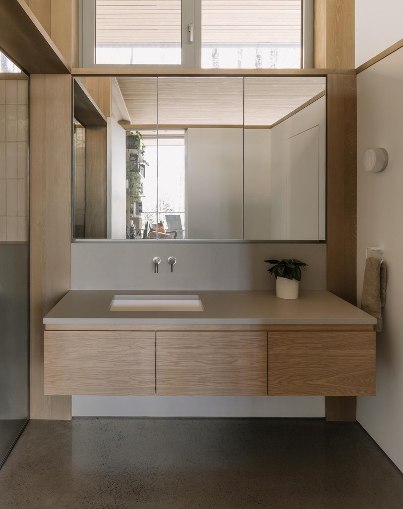 Floating vanity with timber base and mirrored medicine cabinet reflecting a window and potted plant beyond