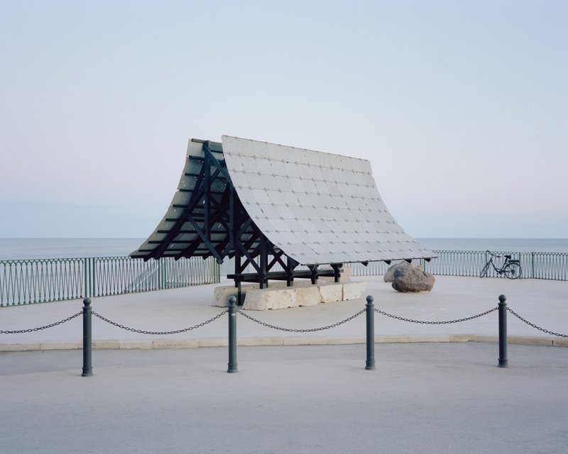 Timber pavilion with white tiled roof and exposed frame on a coastal promenade at dusk