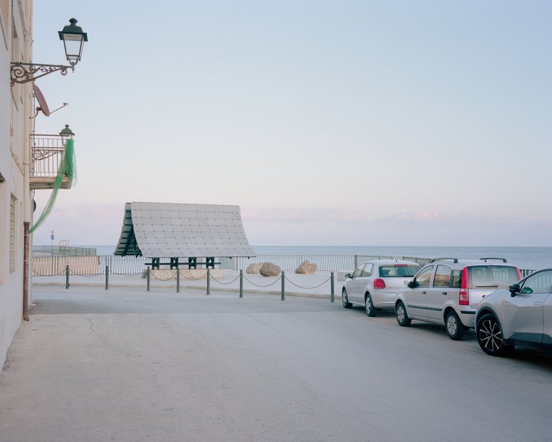 Street view of the pavilion framed by wrought iron balconies and parked vehicles at sunset