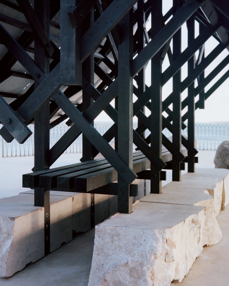 Base detail of the dark timber frame anchored to rough limestone blocks on a concrete terrace