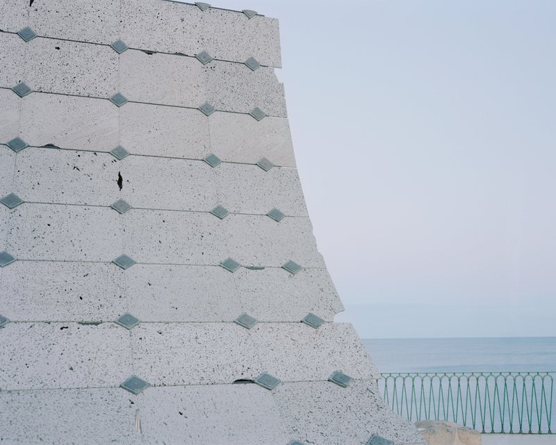 Corner of the tilted concrete wall with metal fixings overlooking a pale blue sea horizon