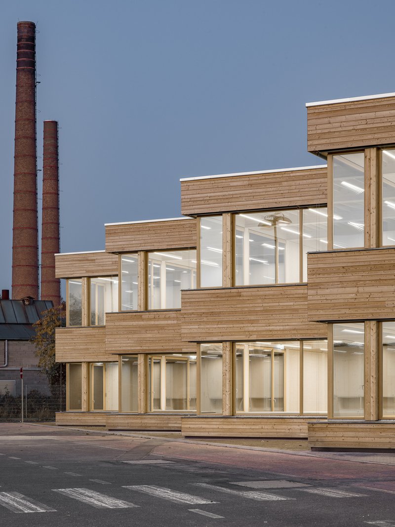 Terraced wood cladding and floor-to-ceiling glazing with industrial chimneys in the background