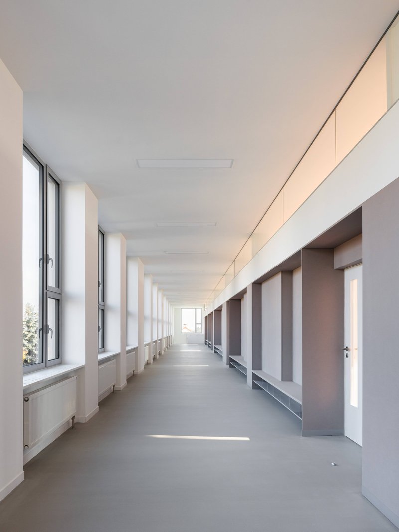 Long corridor with rhythmic window openings on the left and a series of recessed doorways and built-in benches on the right