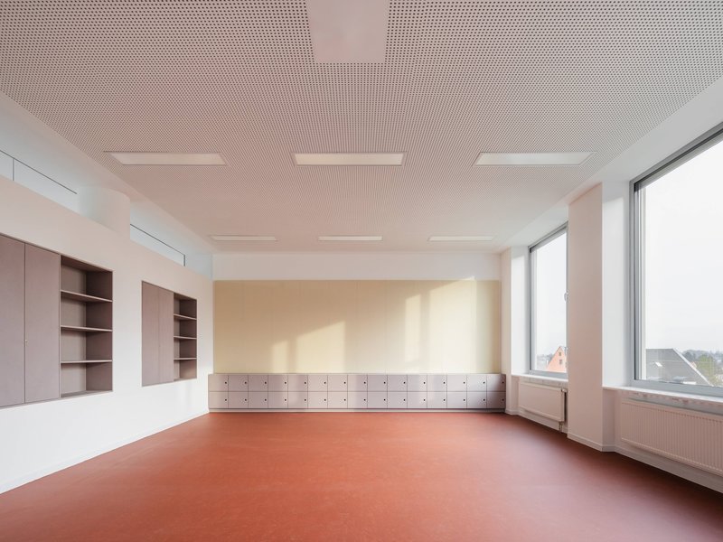 Classroom interior with perforated acoustic ceiling, built-in storage and terracotta rubber flooring in soft daylight