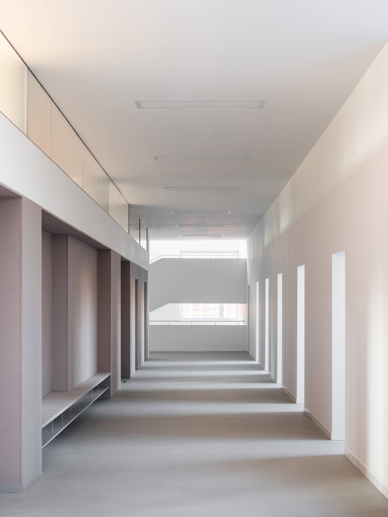 White corridor with rhythmic recessed alcoves along the left wall and daylight filtering from the far end