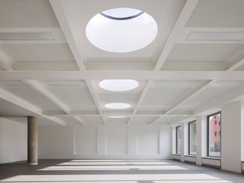 Interior hall with coffered ceiling featuring circular skylights and sunlight casting patterns across the floor