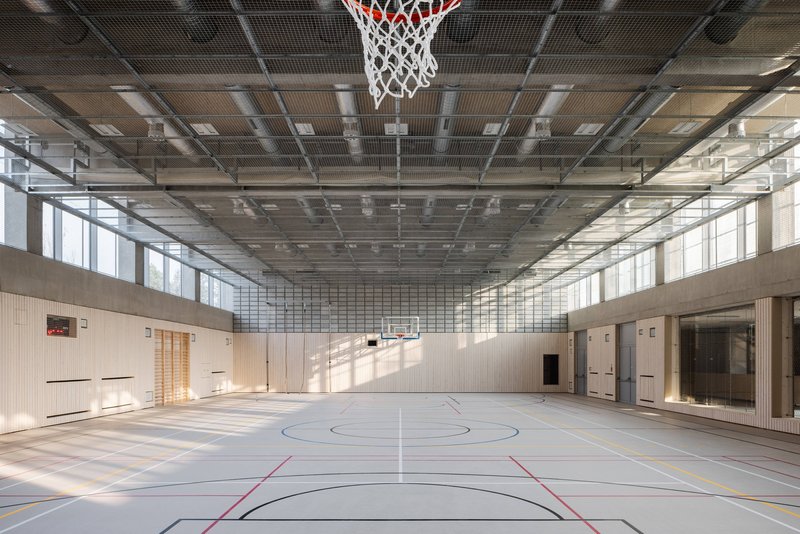 Sports hall with exposed metal grid ceiling and timber wall panels along the perimeter