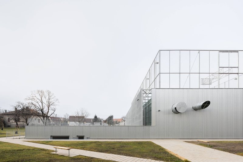 Corrugated metal facade with circular openings across a winter lawn with bare trees