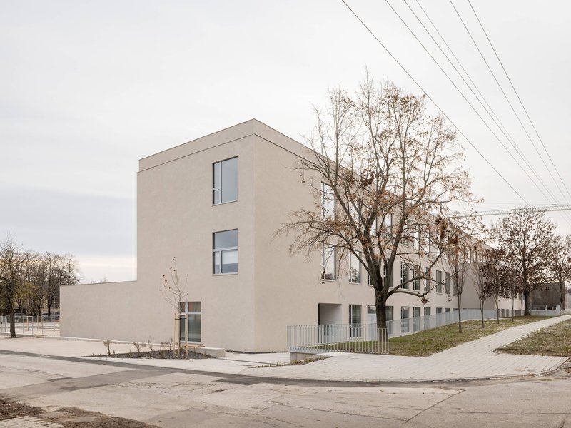 Three-storey rendered plaster block with vertical window strips under bare winter trees