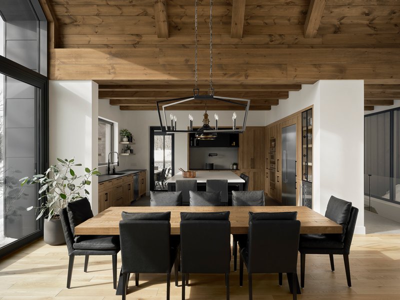 Open dining area with exposed timber ceiling beams and black metal pendant light above wood table