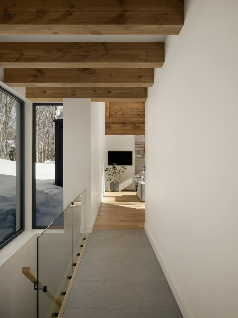 White corridor with exposed timber ceiling beams and glass balustrade overlooking snowy exterior
