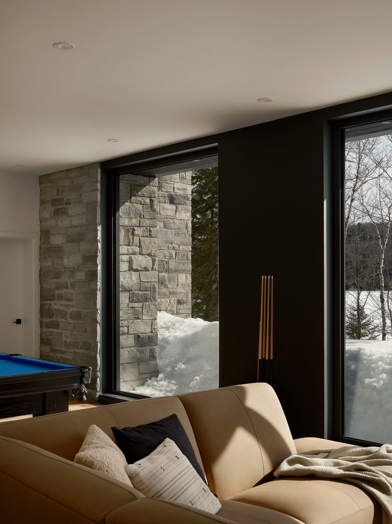 Corner lounge with black-framed glazing beside textured stone wall in winter sunlight